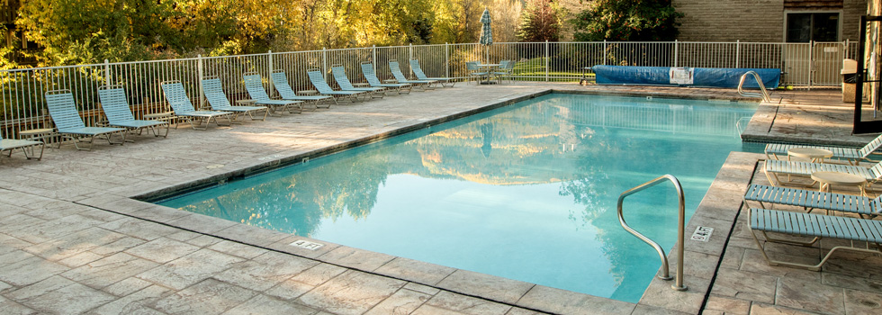 A rectangular pool with lounge chairs and a fence, surrounded by trees.
