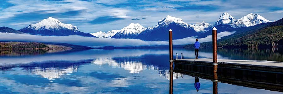 Person standing on a pier at a mountain lake, looking at snow capped mountains around Sandstone Creek Club, Hotel and Timeshares in Vail, Colorado